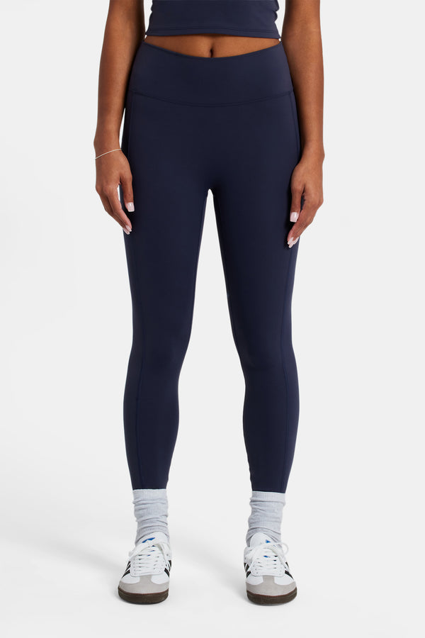Female model wearing deep waist band leggings in navy with white background 