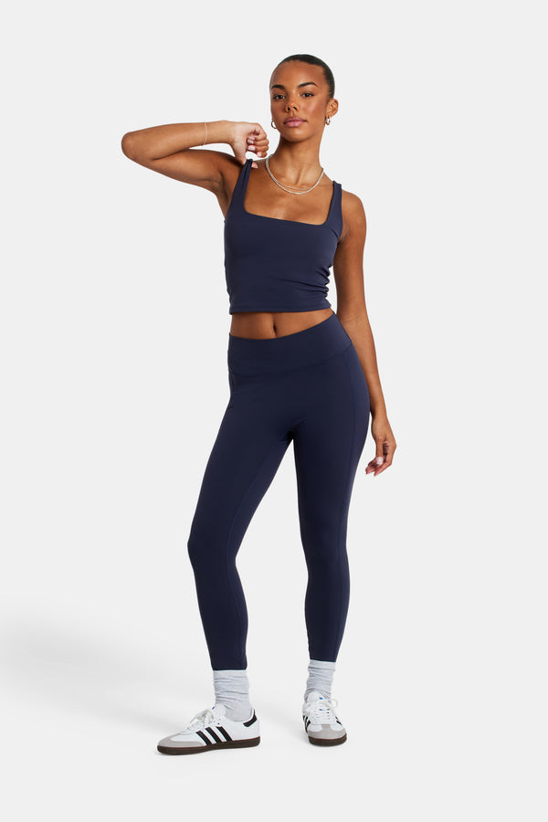 Female model wearing deep waist band leggings in navy with white background